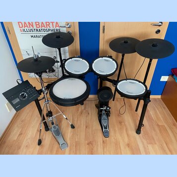Elektronická bicí souprava s černými pady a činely. Na všech bílých plochách padů je vidět nápis Roland V-Drums. Součástí sestavy je ovládací modul,…
