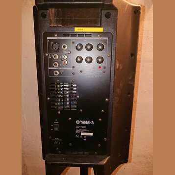 Zadní strana černého aktivního reproduktoru značky YAMAHA. V horní části je ovládací panel s vstupy INPUT, sekcí EQ a regulátorem LEVEL, nad kterým j…