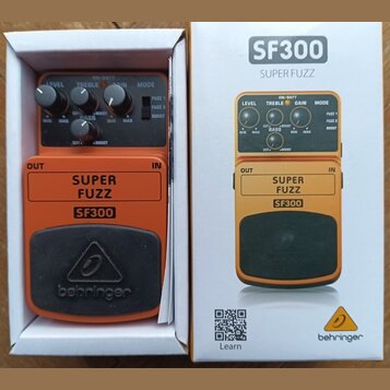 Fotografie zobrazuje oranžový kytarový efekt SF300 SUPER FUZZ značky behringer v původním bílém krabici. Pedal má čtyři ovládací knoflíky s nápisy LE…