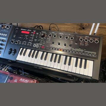 Černý syntezátor s klaviatura značky Roland, model JD-Xi. Horní panel obsahuje červený displej, početné ovládací knofíky a tlačítka rozdělená do sekc…