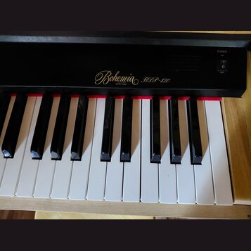 Černý digitální piano s bílými a černými klávesami. Na černé ovládací liště je zlatý nápis Bohemia DIGITAL PIANO a model BDP-130. V pravé části je vy…