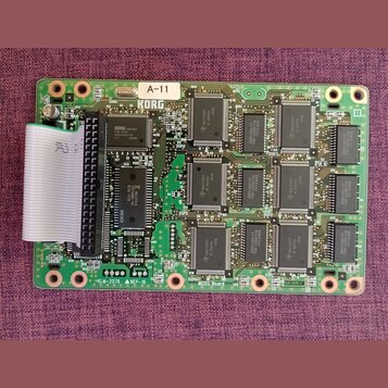 Zelená tiskovaná deska s osazenými integrovanými obvody a elektronickými součástkami. V horní části je bílá nálepka s nápisem A-11 a pod ní logo KORG…