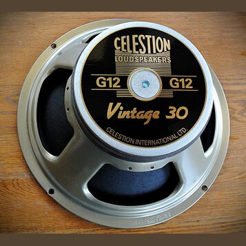 Reproduktor s kovovým rámem stříbrné barvy a černým krytem magnetu. Na krytu je zlatý nápis CELESTION LOUDSPEAKERS, G12 G12 a Vintage 30, v dolní čás…