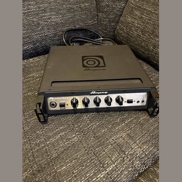 Černý basový zesilovač značky Ampeg s nápisem PortaFlex. Na horní straně je umístěno logo Ampeg. Přední panel obsahuje ovládací knofíky, přepínač -15…