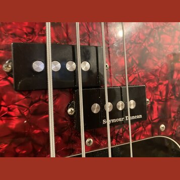 Detailní záběr na dvě černé humbuckery na basové kytáře s červeným perleťovým povrchem. Na spodním snímači je bílý nápis Seymour Duncan. Oba snímače…