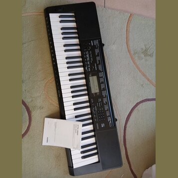 Černý digitální klavír s bílými a černými klávesami. Na ovládacím panelu je nápis CTK-3500 a logo CASIO. K nástroji přikládaný papírový dokument nese…