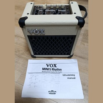 Kremový kytarový kombo zesilovač s černou mřížkou reproduktoru a nápisem VOX na přední straně. Na horním ovládacím panelu jsou různé přepínače a pote…