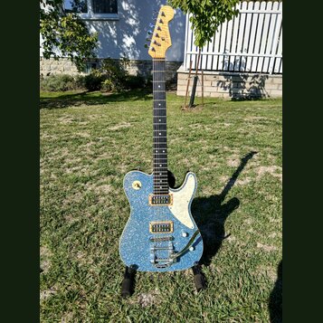 Elektrická kytara s modrým třpytivým povrchem těla a bílým pickguardem. Na hlavě hředu je viditelné logo Fender. Kytara má dva humbuckery, jeden ovlá…