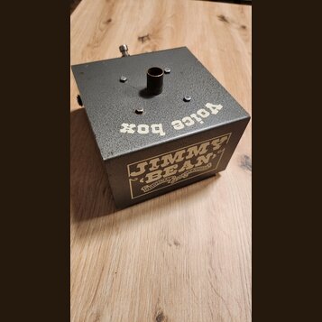 Šedý kovový efekt pedál s texturou povrchu. Na horní straně je nápis voice box a na boční straně náleplka s textem JIMMY BEAN ORIGINAL AND GENUINE. U…