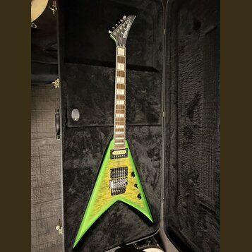 Zelená elektrická kytara s tělem ve tvaru V, položená v černém tvrdém kufru. Na hlavě je bílý nápis Jackson. Kytara má dva humbuckery, šest strun a h…