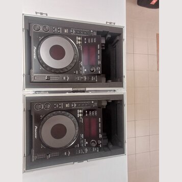 Dvě černé CDJ jednotky značky Pioneer umístěné v transportním kufru s hliníkovým profilem. Na obou zařizeních je viditelné logo Pioneer a nápis CDJ-1…