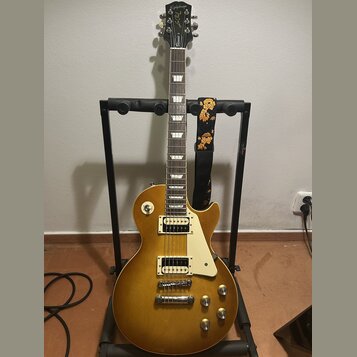Elektrická kytara s žlutým gradientním lakem v provedení singlecut, umístěná na černém stojanu. Na hlavě je nápis Epiphone a logo Les Paul Custom. Ky…