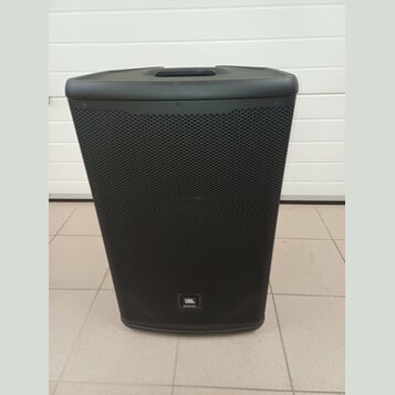 Černý reproduktor s kovovou mřížkou a integrovanou rukojetí v horní části. Ve spodní části je umístěno logo JBL. Povrch vypadá čistě a bez viditelnýc…