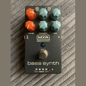 Černý efekt pedál s nápisem bass synth a logem MXR BASS INNOVATIONS. Zařízení má šest ovládacích knoflíků v oranžové a modré barvě, stříbrný spínací…
