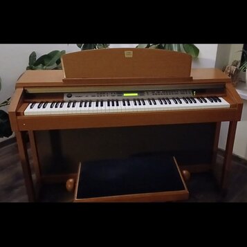 Digitální piano v dřevěné barvě s bílými a černými klávesami. Na horní části je nápis Yamaha. Nástroj má ovládací panel s tlačítky a malým displejem,…