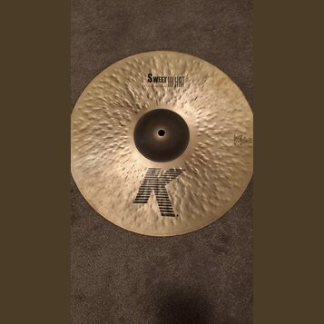 Zlatavý kovový činel s kladivkovaným povrchem. Na povrchu jsou černé nápisy SWEET HI HAT a 15"/38 cm BOTTOM, v dolní části velké logo K a vpravo nápi…