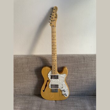 Světle hnědá elektrická kytara s přírodním povrchem dřeva a bílým perleťovým pickguardem. Na hlavě hředu je černý nápis Fender TELECASTER. Tělo kytar…