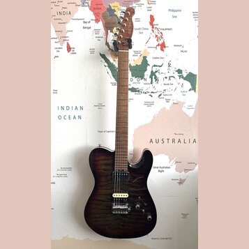 Elektrická kytara s tmavě hnědým, žilnatým povrchem těla a hnedým hnedým hřidnicí. Na hlavě je viditelné logo "Ibanez". Nástroj má dva humbuckery s k…