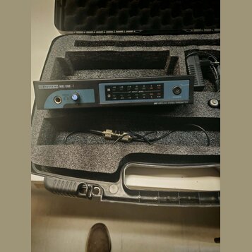 Černý přenosník s nápisem LD SYSTEMS MEI ONE -T a doplňkovým označením UHF WIRELESS STEREO TRANSMITTER. Zařízení má na přední straně dva LED indikáto…