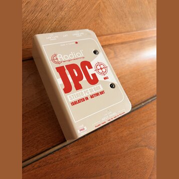 Béžová DI box s nápisem Radial engineering a červeným označením JPC MK3. Na spodní části je text STEREO PC DI BOX a ISOLATED IN · ACTIVE OUT. V dolní…