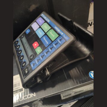 Černý procesor vokalových efektů s dotykovým displejem a ovládacími prvky. Na horní části je nápis TC HELICON a model VOICELIVE Touch. Displej obsahu…