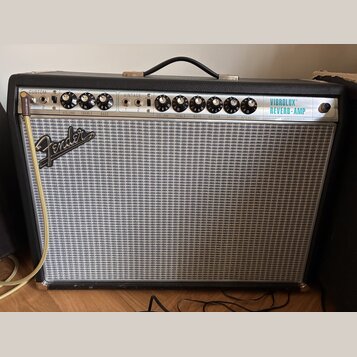 Kytarový kombo zesilovač s černým krytím a stříbrnou síťovkou. Na horním ovládacím panelu jsou nápisy CUSTOM a VINTAGE, značka Fender na přední stran…