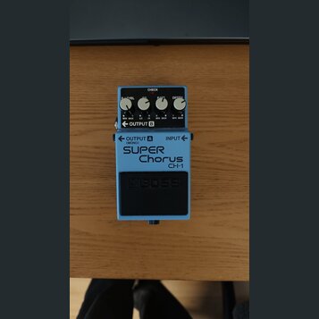 Modrý efekt pedál s černým spínacím tlačítkem. Na přední straně je bílý nápis SUPER Chorus CH-1 a v dolní části logo BOSS. Horní panel obsahuje čtyři…