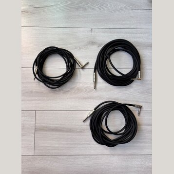 Tři černé audio kabely s kovovými konektory typu jack. Kabely jsou svinuté do klubíčků a položené na světlém laminátovém povrchu. Na konektorech nejs…
