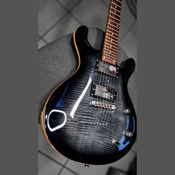 Elektrická kytara s tmavým, žilnatým povrchem těla a hnědým hnedlecem. Nástroj má dva humbuckery, fixační most a tři ovládací knoflíky. Na těle nejso…