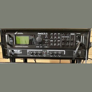 Černý rack s dvěma zařízeními. Horní jednotka má nápisy FRACTAL AUDIO SYSTEMS a Axe-Fx II XL, dále označení PREAMP/EFFECTS PROCESSOR, displej a řadu…