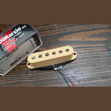 Kremově bílý humbucker s šesti viditelnými póly, vedoucími z něj čtyři barevné vodiče (červený, bílý, zelený a černý). Vedle nástroje je umístěna kra…