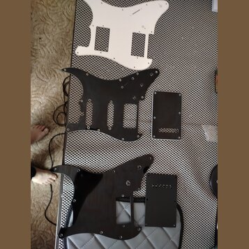 Na fotografii jsou třipickguardy pro elektrickou kytaru a dvě doprovodné krytky. Horní pickguard je bílý, prostřední a spodní jsou černého provedení.…