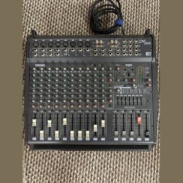 Černý mixovací pult s nápisy YAMAHA a EMX 2000. Zařízení obsahuje početné vstupní kanály s potenciometry, přepínači a posuvníky. V pravé části je umí…