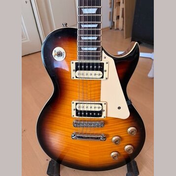 Elektrická kytara s tónem sunburst (oranžová a hnědá) a krémovým plechtrzem. Nástroj má dva humbuckery s bílými rámečky, chromovaný most a stopku. Na…