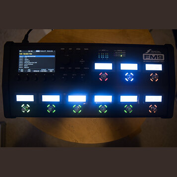 Černý procesor efektů Fractal Audio Systems FM9 Amp Modeller / FX Processor Mark II. Zařízení má LCD displej s textem „518: Derelict Tele“, několik p…