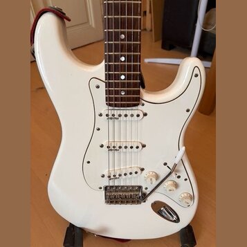 Bílá elektrická kytara typu Stratocaster s bílým pickguardem a hnědým hmatníkem. Nástroj má tři snímače typu single-coil, tři ovládací knoflíky a třy…