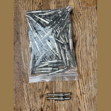 Průhledný plastový sáček plný kovových 6,3mm jack konektorů stříbrné barvy. Pod sáčkem na dřevěném povrchu leží dva stejné konektory vedle sebe. Na k…