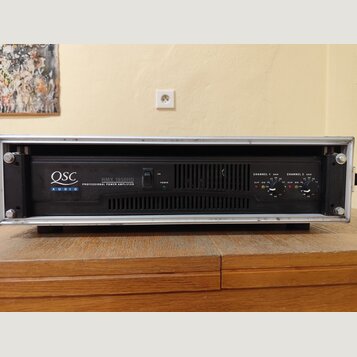 Černý výkonový zesilovač v hliníkovém racku. Na předním panelu je bílý nápis QSC AUDIO a model RMX 1850HD PROFESSIONAL POWER AMPLIFIER. Vpravo jsou o…