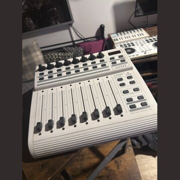 Bílý USB MIDI kontrolér s osmi posuvníky a řadou otočných knoflíků v horní části. Na pravé straně jsou umístěna tlačítka a nápisy B-CONTROL, MIDI FAD…
