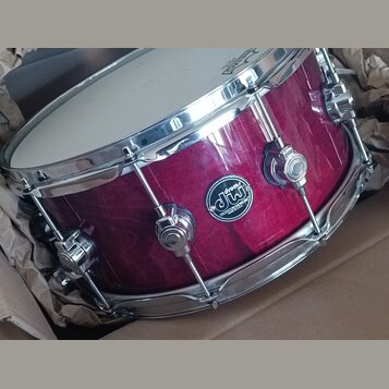 Kolaudovaný buben v tmavě červené barvě s kovovými obručemi a ladicími šrouby. Na korpusu je oválný černý štít s bílým nápisem „dw drums“ a textem „M…