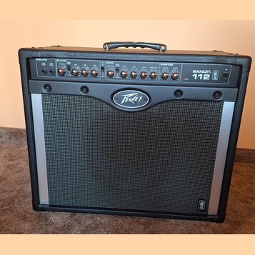 Černý kytarový kombo zesilovač s kovovou stříbrnou mřížkou. Na přední straně je nápis BANDIT 112 a logo Peavey. Horní ovládací panel obsahuje sekce I…