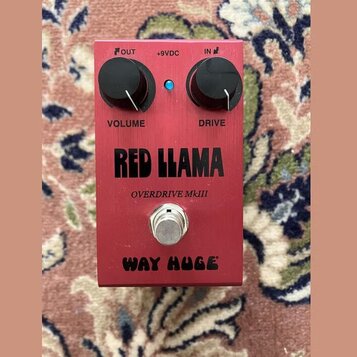 Červený kytarový efekt s nápisy RED LLAMA, OVERDRIVE MkIII a WAY HUGE. Na horní straně jsou dva černé otočné knoflíky s popisky VOLUME a DRIVE, modrá…