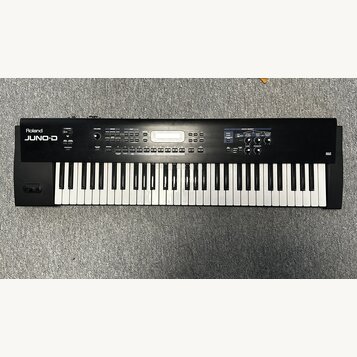 Černý digitální klavír s bílými a černými klávesami. Na levé straně je bílý nápis Roland JUNO-D. Horní panel obsahuje displej, několik tlačítek a oto…
