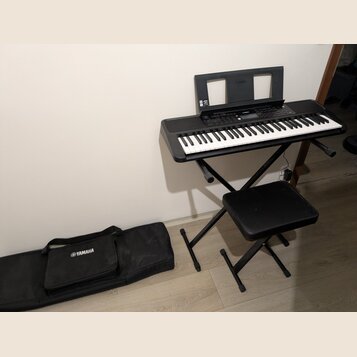 Černý digitální klavír umístěný na černém skládacím stojanu s přívodním kabelem. Na nástroji je vidět nápis YAMAHA a doprovodná hudební notová opěrka…