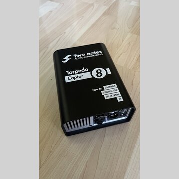 Černý kovový box s nápisy Two notes AUDIO ENGINEERING a Torpedo Captor 8. Na boku jsou uvedeny funkce 100W 8Ω LOADBOX, ATTENUATOR, SPEAKERSIM a DI. Z…