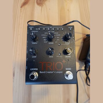 Černý efekt pedál s nápisem TRIO+ a Band Creator™+ Looper. Zařízení má tři ovládací knoflíky označené jako TEMPO, GENRE a STYLE, s dopisky LOOP, BASS…