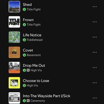 Snímek zachicuje seznam skladeb v digitální aplikaci na černém pozadí. Jsou zde uvedeny názvy písní a interpretů: Shed (Title Fight), Frown (Title Fi…