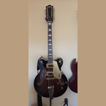 Polodublová elektrická kytara s tmavě hnědým gradientním povrchem a f-otvory. Na hlavě i na plechovce je viditelné logo GRETSCH, hриф má bílé vložky.…