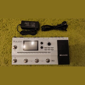 Bílý kytarový procesor s černým pedálem, na kterém je nápis MOOER. Na horní části přístroje je displej a text VCE 250 amp modelling & multi-fx. Vedle…