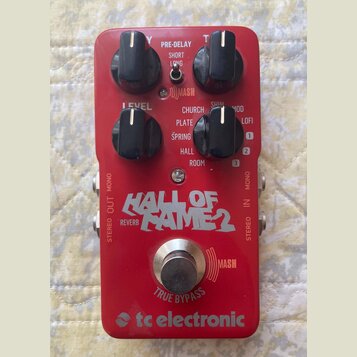 Červený kytarový efekt s nápisem HALL OF FAME 2 REVERB a logem tc electronic. Zařízení má čtyři černé otočné ovratky s popisky LEVEL, PRE-DELAY (SHOR…